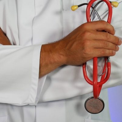 Doctor in a white lab coat with crossed arms holding a red stethoscope